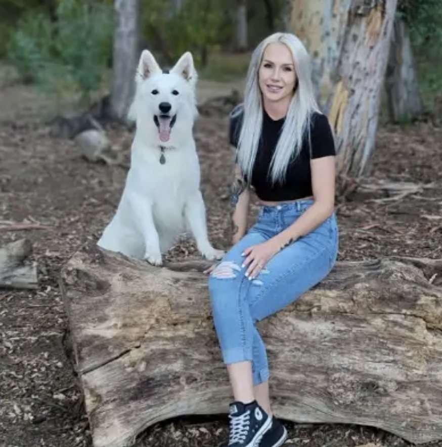 Nicole sitting on a log with Neo, her white Berger Blanc Suisse